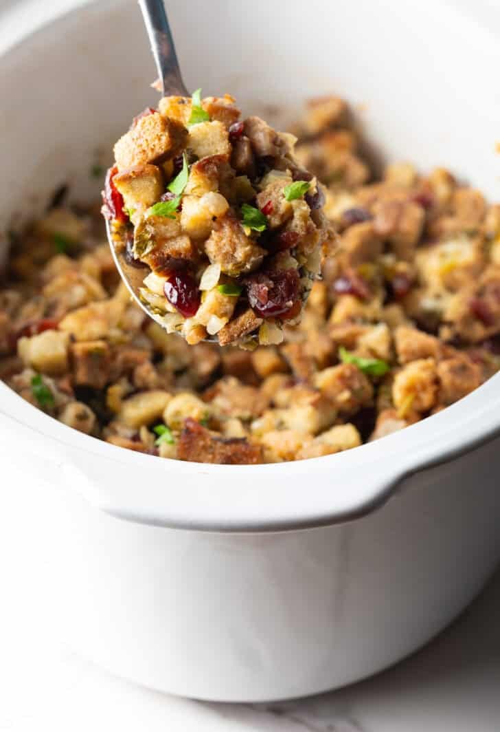 A scoop of slow cooker stuffing being held with a metal spoon.