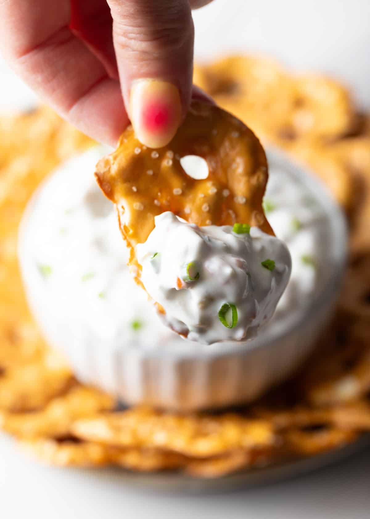 Hand holding a pretzel with a scoop of olive dip to camera.