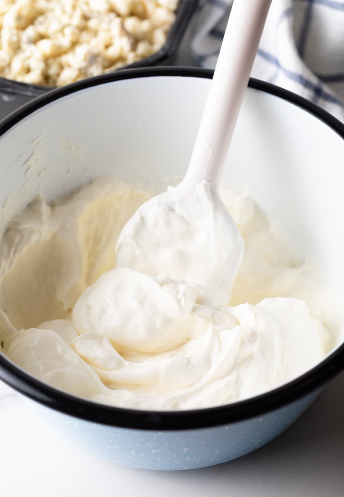 White bowl with cream cheese and olive dip, stirred with a white spatula.