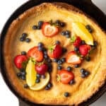 Top down view Dutch baby in a cast iron skillet, topped with strawberries, blueberries, and lemon slices.