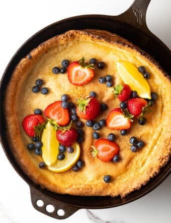 Top down view Dutch baby in a cast iron skillet, topped with strawberries, blueberries, and lemon slices.