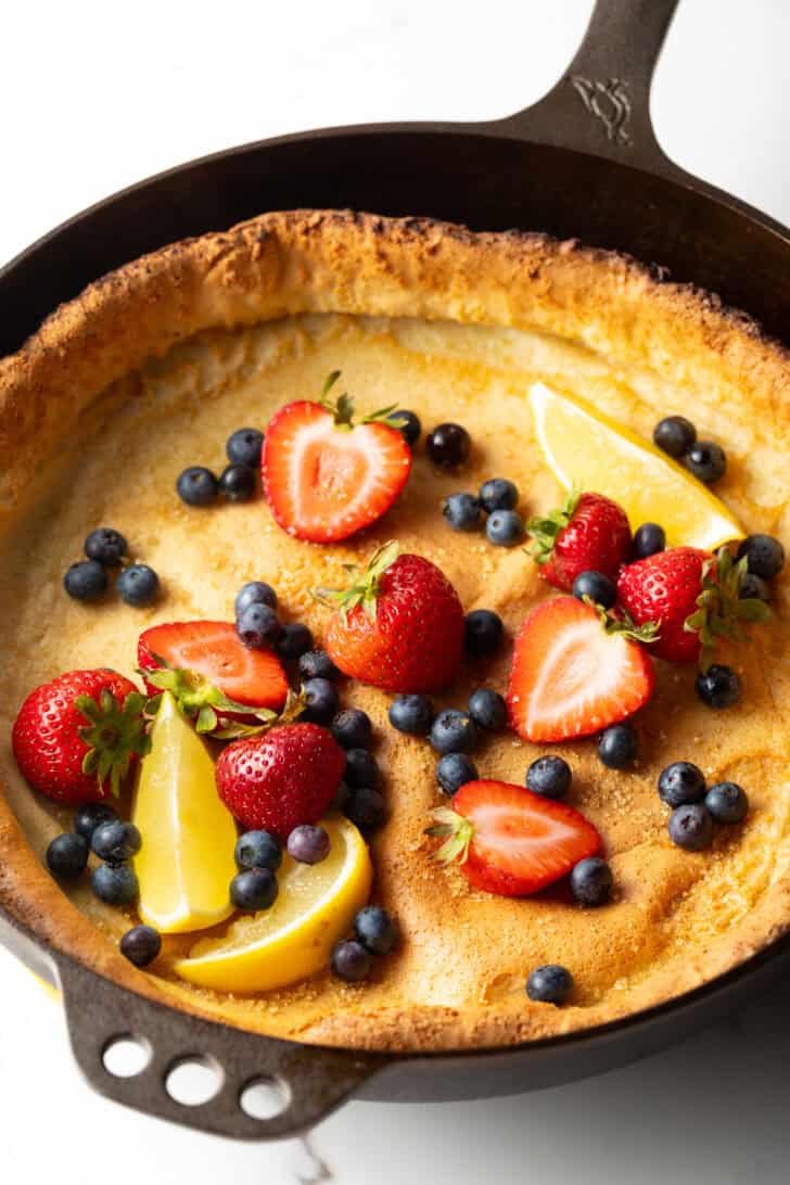 Dutch baby in a cast iron skillet, topped with strawberries, blueberries, and lemon slices.