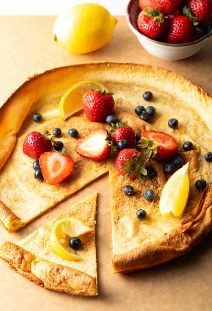 Dutch baby on a cutting board, topped with strawberries and blueberries, with a slice pulled aside.