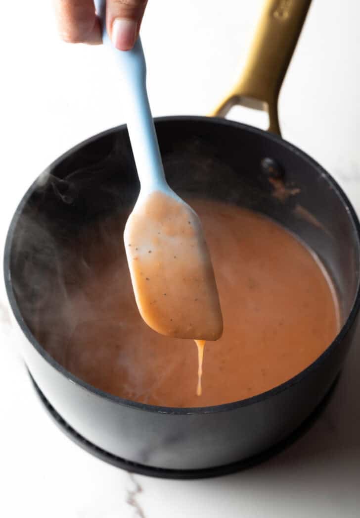 Easy gravy recipe dripping off of a spatula over a black pot.