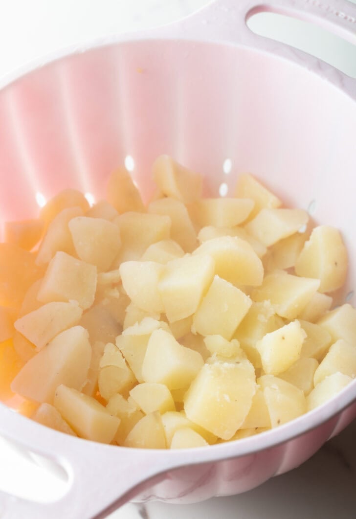 A white colander straining cooked potatoes.