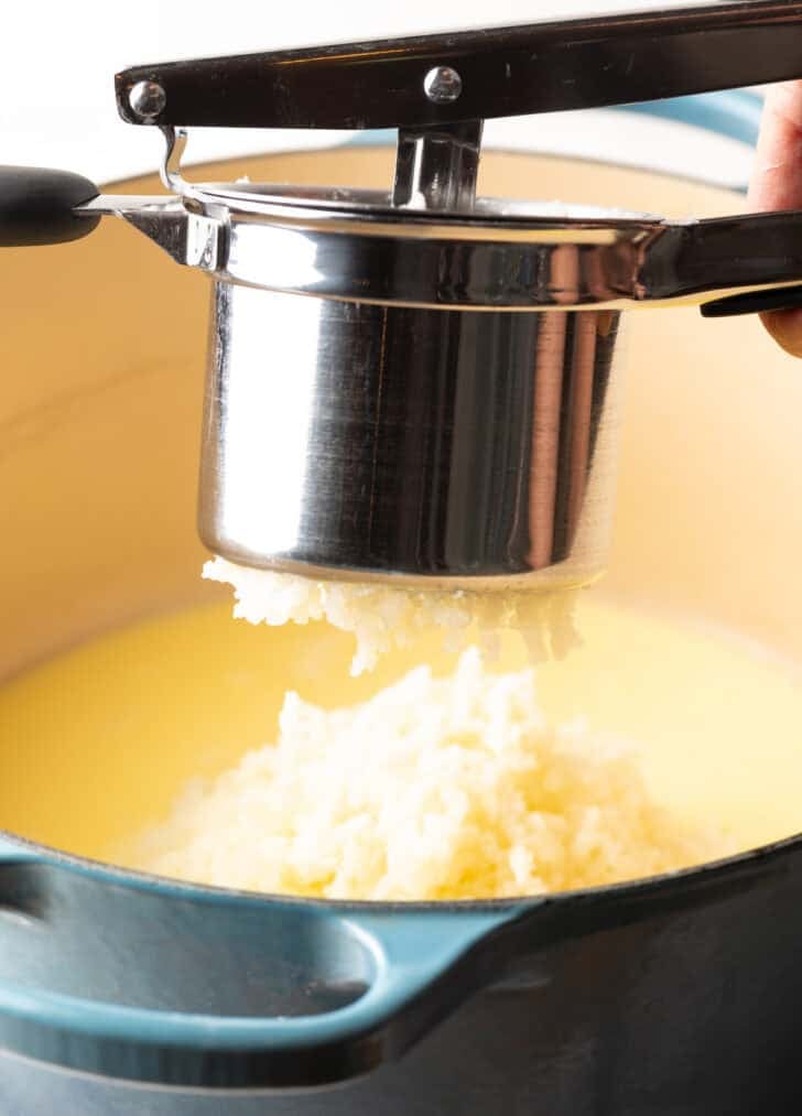 A potato ricer ricing mashed potatoes into a pot.