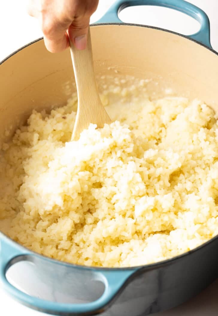 A wooden spoon stirring freshly riced potatoes.
