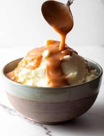Easy mashed potatoes and gravy with homemade brown gravy being spooned over the mashed potatoes.