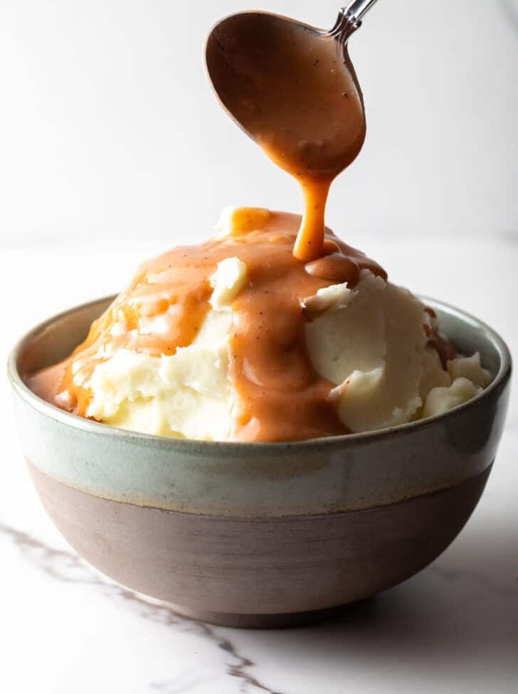 Easy mashed potatoes and gravy with homemade brown gravy being spooned over the mashed potatoes.