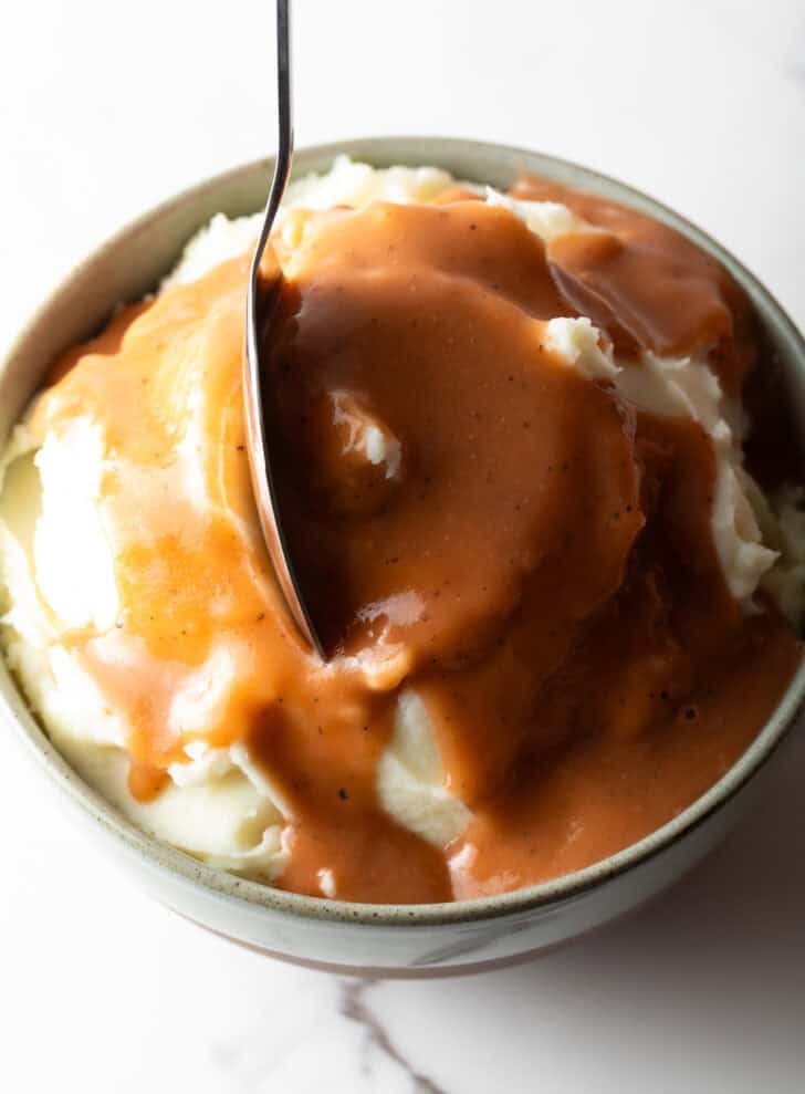 A bowl of mashed potatoes drenched in brown gravy with a spoon dipping into the bowl.