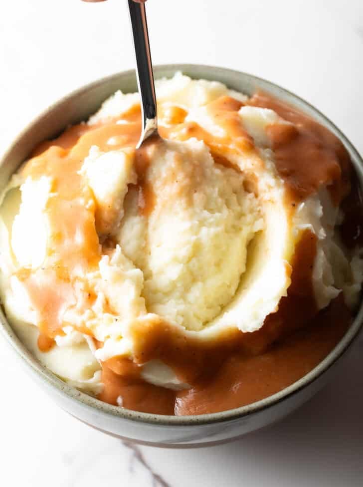 A spoon scooping a bite of easy mashed potatoes and gravy from a bowl.