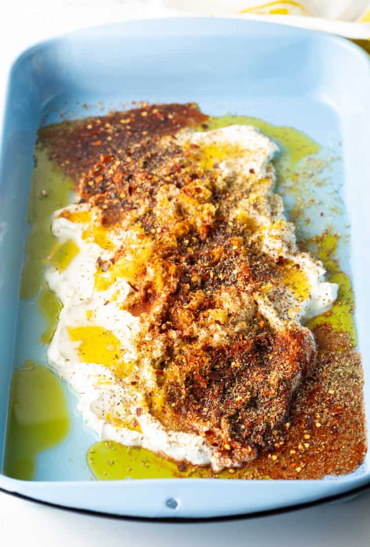 Combination of yogurt, olive oil, and greek spices in a blue rectangle baking dish.