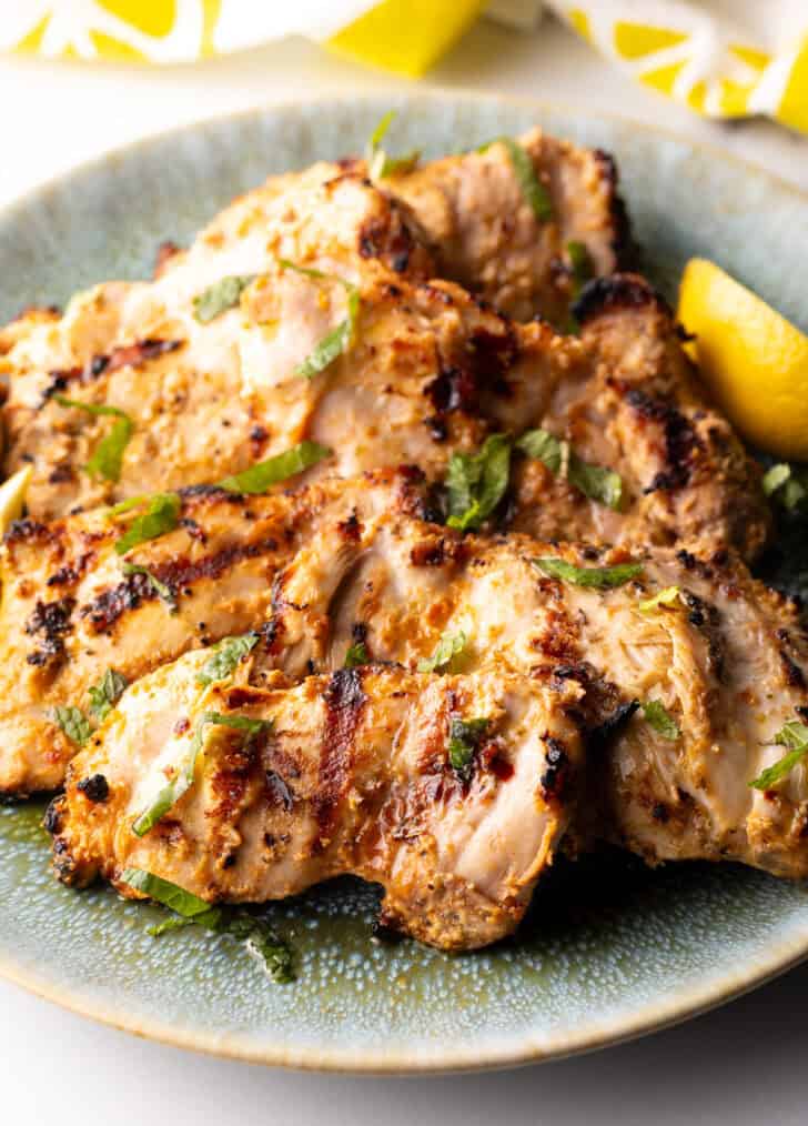 Grilled marinated chicken thighs in a shallow blue bowl.