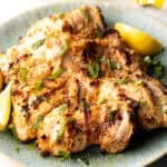 Grilled marinated chicken thighs in a shallow blue bowl.