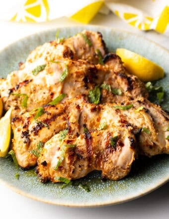 Grilled marinated chicken thighs in a shallow blue bowl.