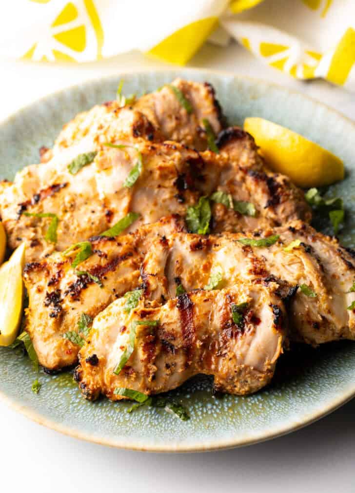 Grilled marinated chicken thighs in a shallow blue bowl.
