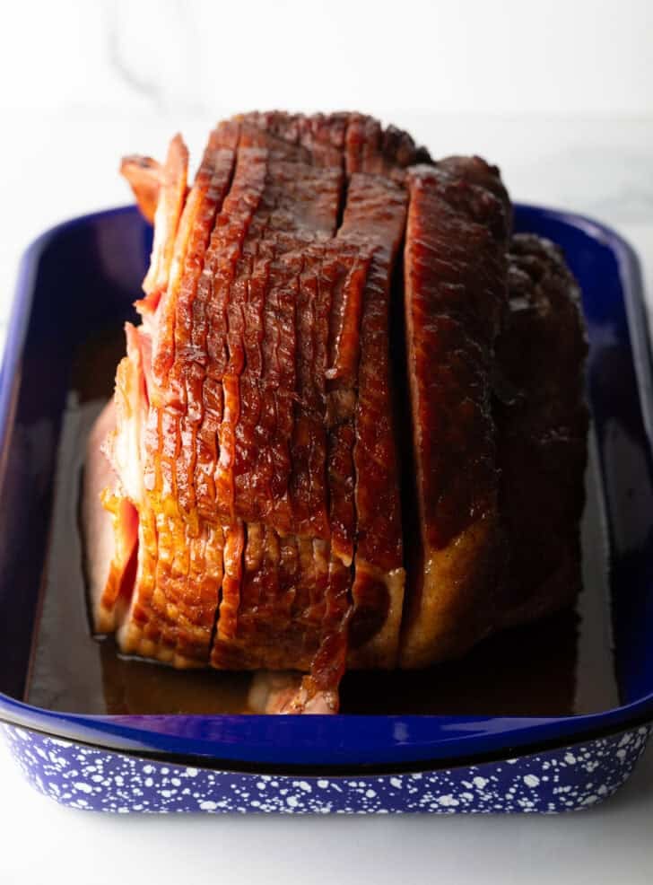 A cooked spiral ham in a blue and white speckled roasting pan.