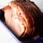 A cooked spiral ham in a blue and white speckled roasting pan.