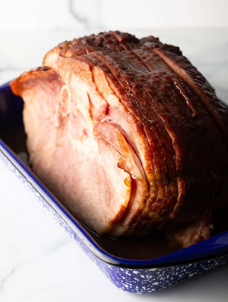 A cooked spiral ham in a blue and white speckled roasting pan.