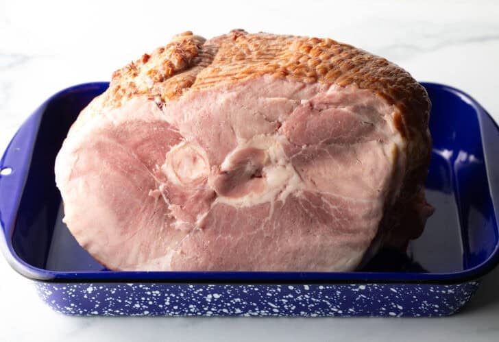 A cooked spiral ham in a blue and white speckled roasting pan.
