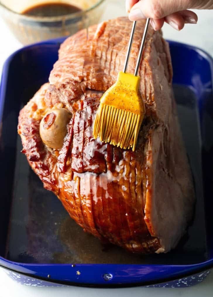 Basting a cooked spiral ham in sauce with a yellow silicone brush.