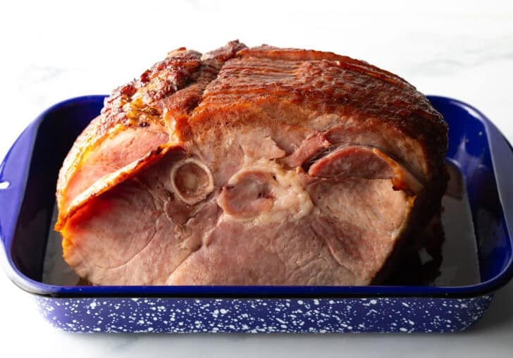 A cooked spiral ham in a blue and white speckled roasting pan.