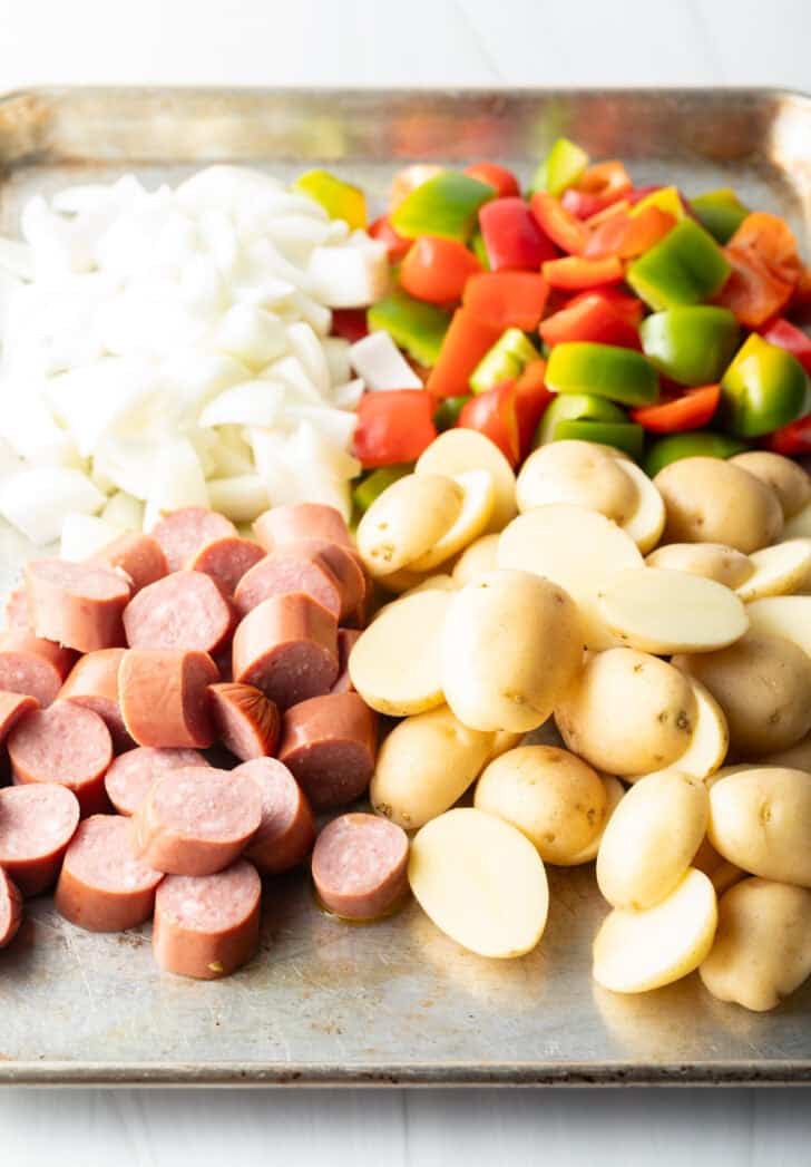 Raw sausage, potatoes, peppers, and onions on a baking sheet.