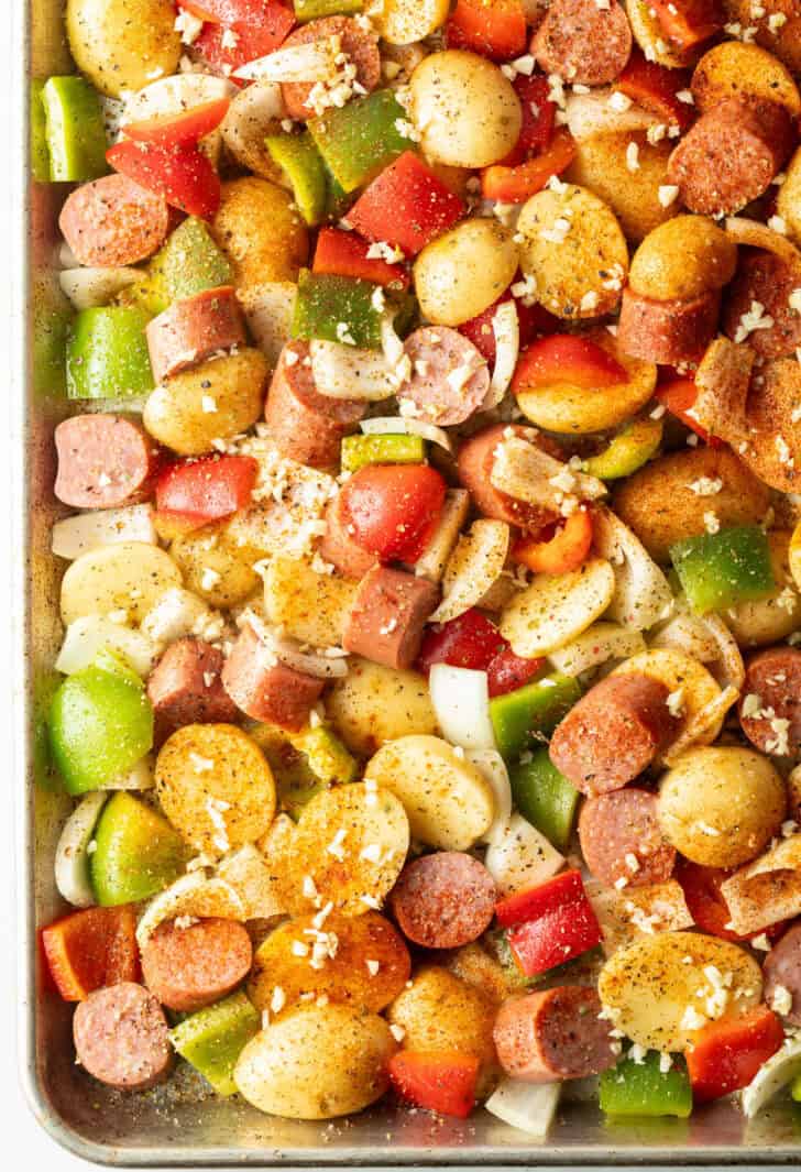 Kielbasa sausage and veggies with seasonings and garlic on a sheet pan.
