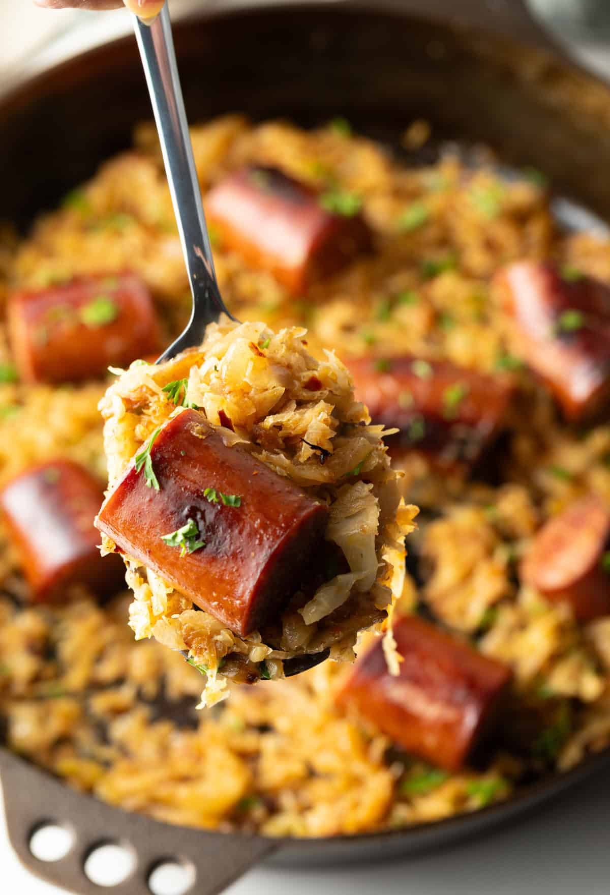 Close view of a piece of cooked sausage on a spoon with sauerkraut.