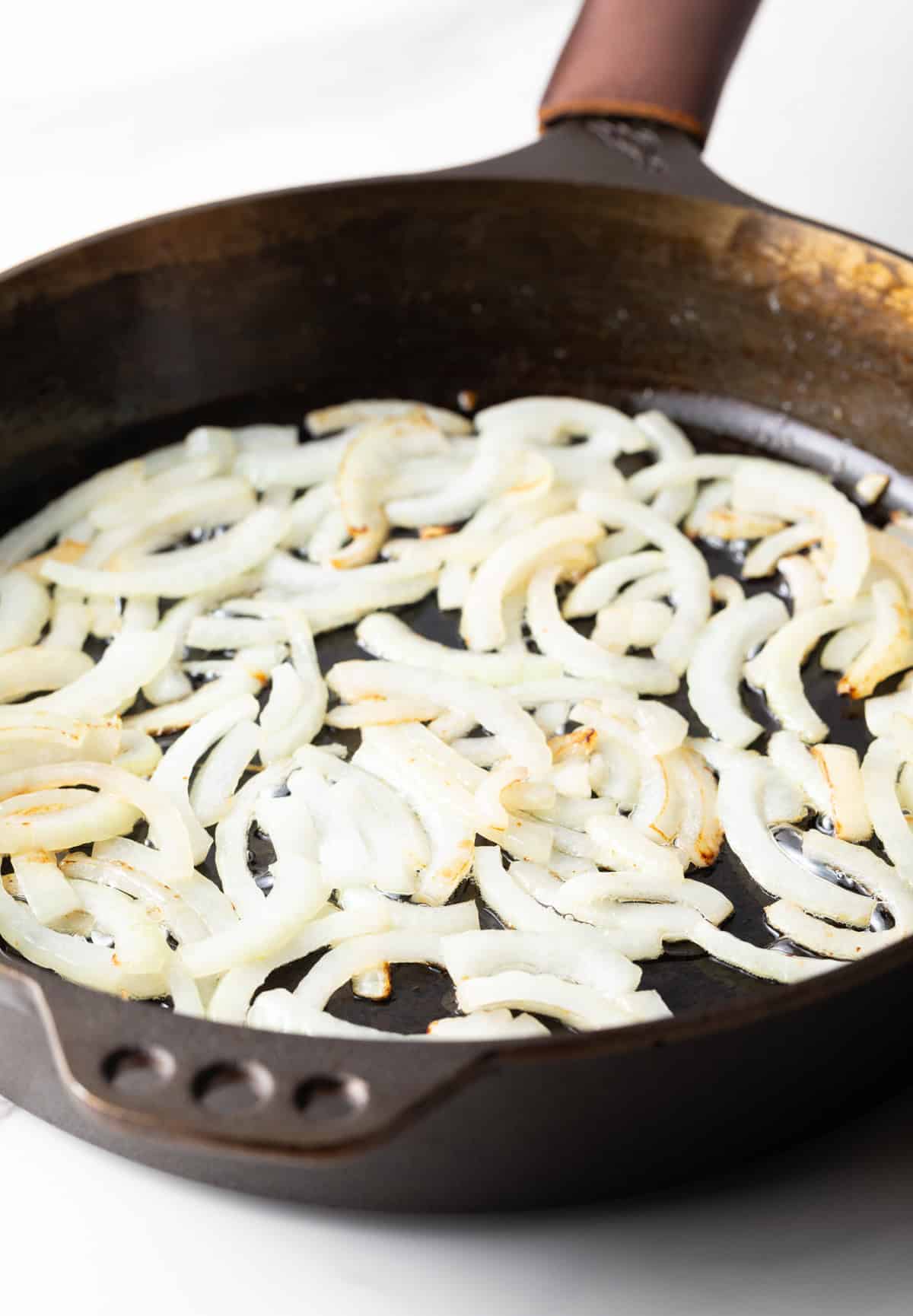 Onion slices sauteeing in a large cast iron skillet.