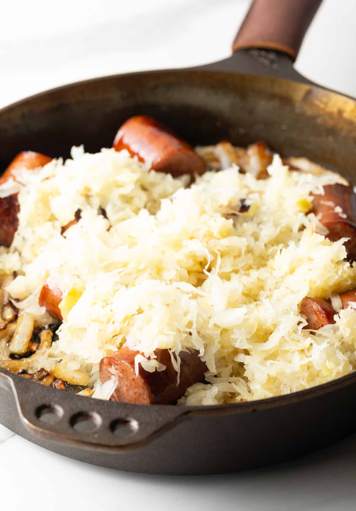 Large skillet with kielbasa pieces on top of sauerkraut.