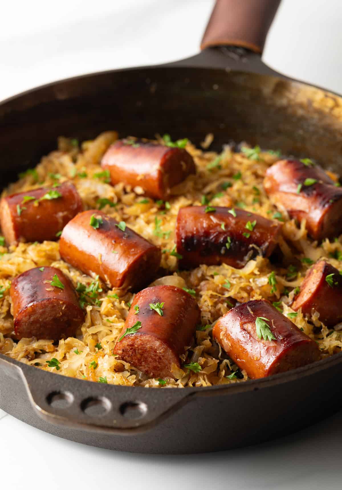 Large skillet with kielbasa pieces on top of sauerkraut.