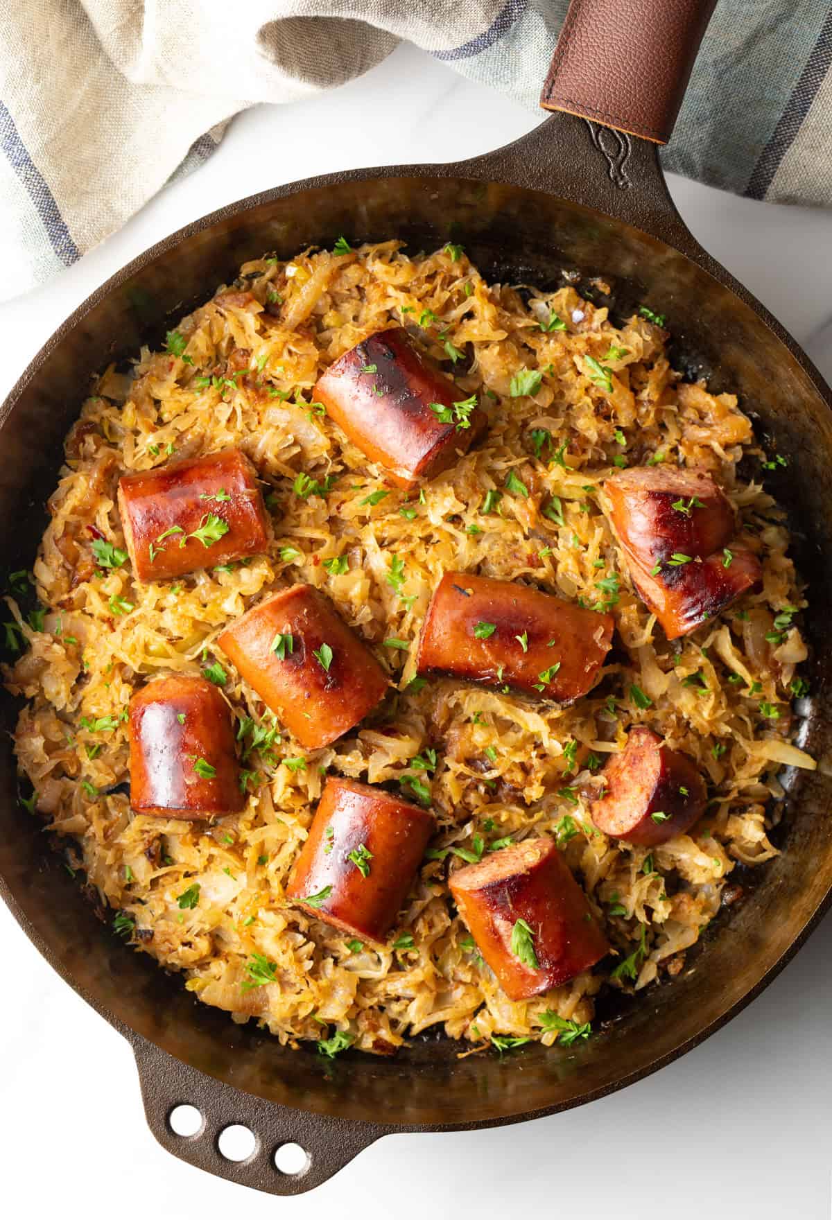 Top down view large skillet with browned sauerkraut and 8 pieces of cooked kielbasa sausage.