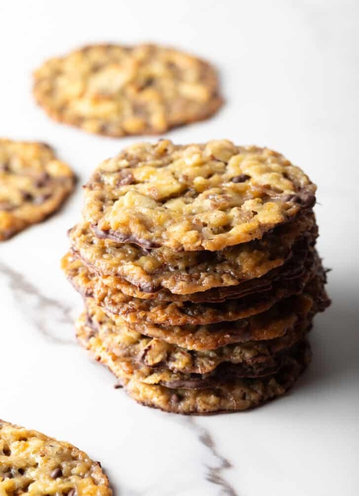 Stack of oatmeal lace cookies on a white marble surface.