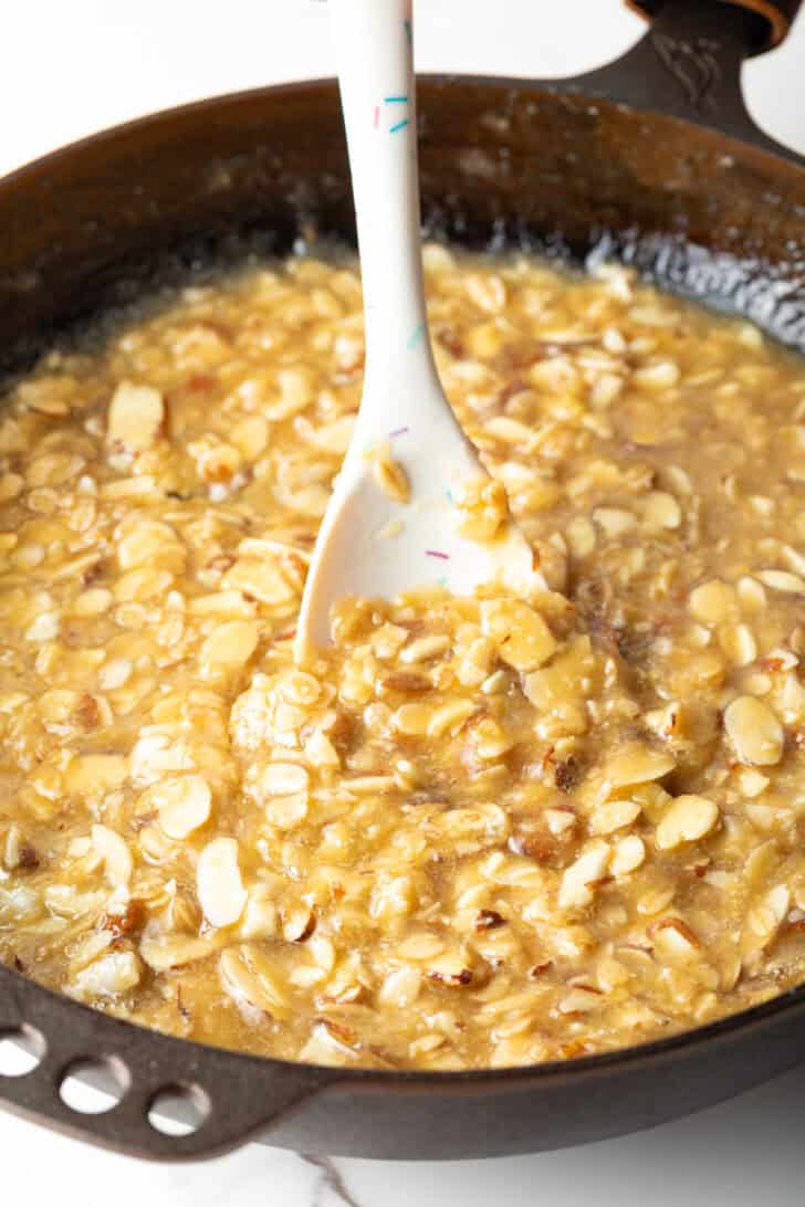 A white spatula is stirring the oatmeal lace cookies mixture in a metal pan.