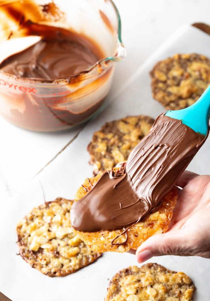 Shot of a single lace cookie with a spatula spreading melted chocolate on the cookie.