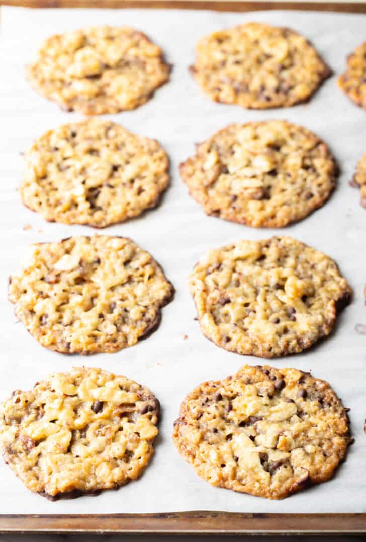 Eight finished Florentine lace cookies lined up on white parchment paper.