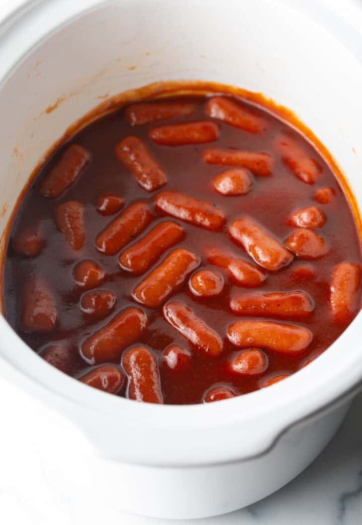 Little smokies in barbecue sauce in a white crock pot.