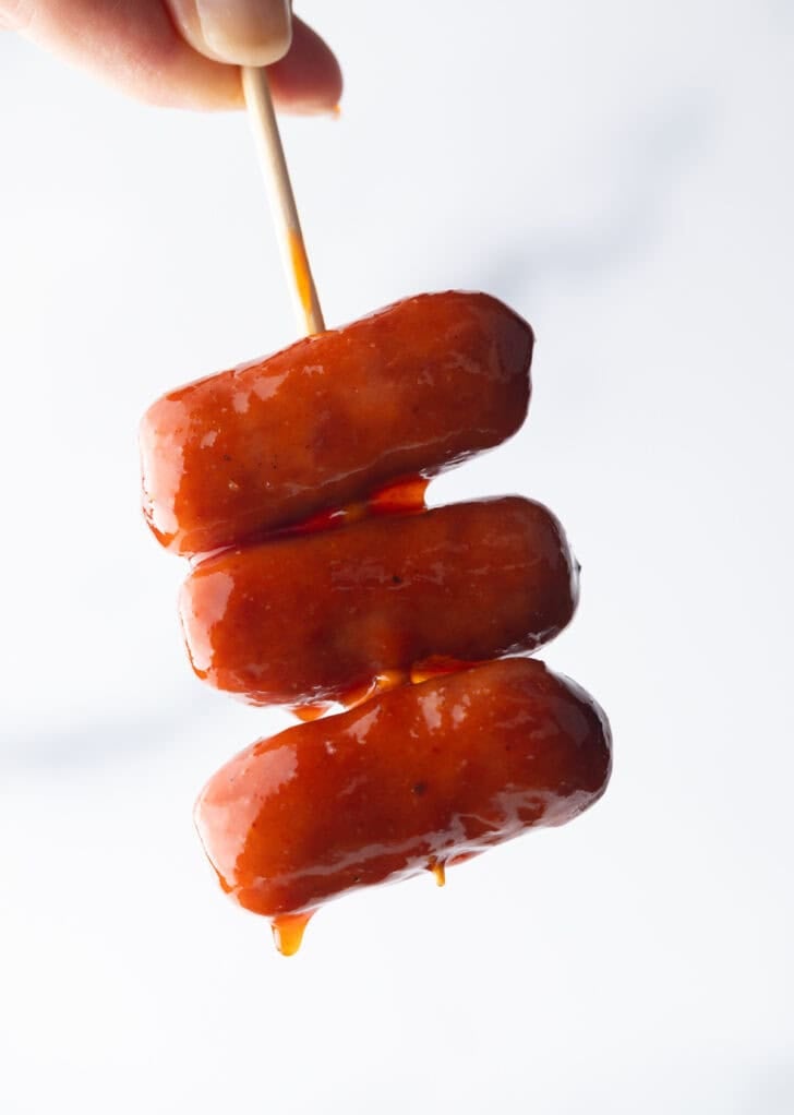 Hand holding a skewer with 3 little smokies.