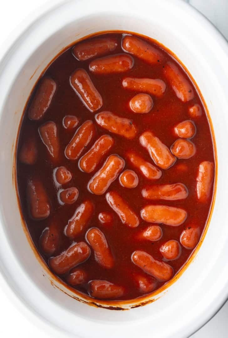 Top down view little smokies in barbecue sauce in a white crock pot.