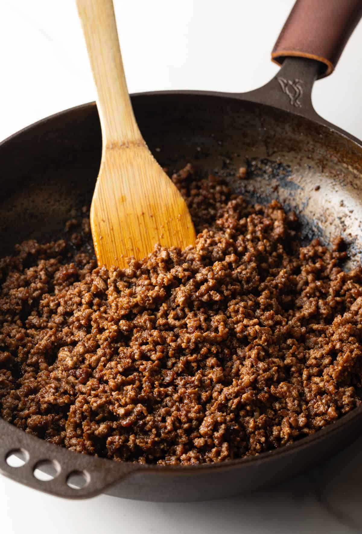 Cooking crumbled ground beef in a large skillet with a wooden spatula.