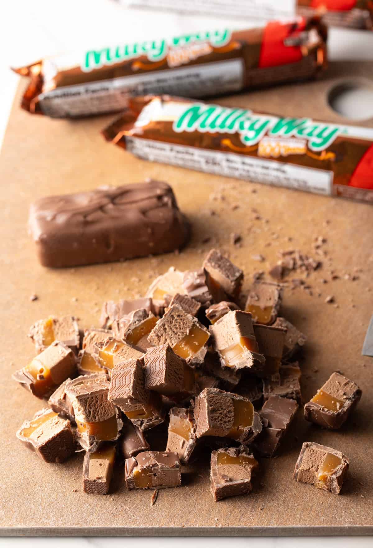 Pieces of chopped Milky Way bars on a wooden cutting board.