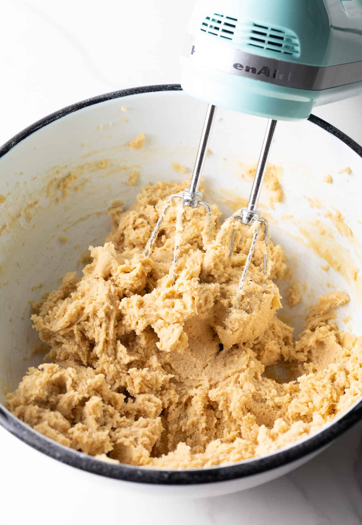 Milky Way cookie dough in a white bowl being blended with a mixer.