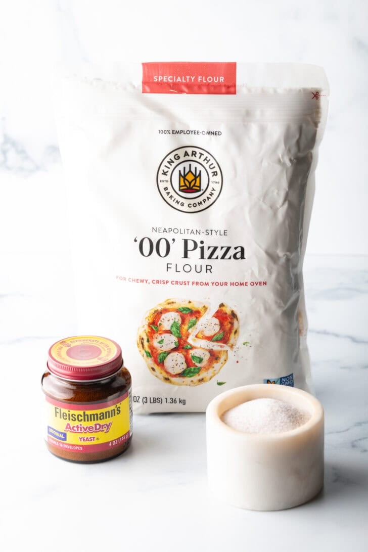 Pizza dough ingredients: Bag of pizza flour, jar of yeast, and white ramekin with salt.
