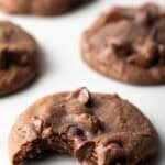 5 baked nutella cookies with chocolate chips on a white background. The closest cookie has a bite taken out of it.