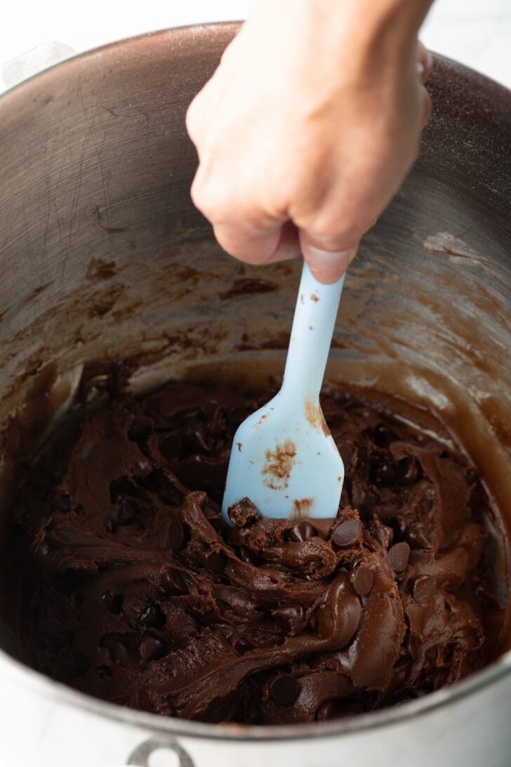 Using a blue spatula to combine nutella cookie ingredients in a large metal bowl.