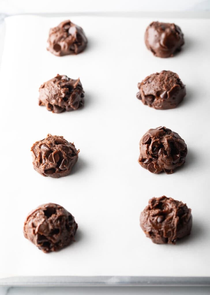 8 balls of chocolate and nutella cookie dough on a baking sheet.