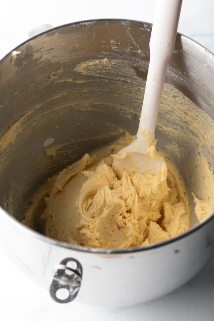 Potato chip cookie batter in metal bowl with white spoon stirring.