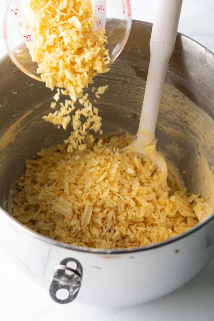 Crushed potato chips being poured over cookie dough.