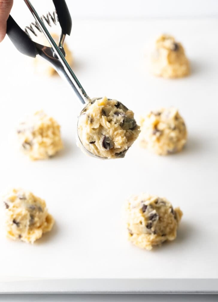 Potato chip cookie dough in metal scoop with cookie dough balls below it.
